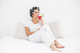 Smiling brunette in hair curlers sitting on her bed drinking a cocktail