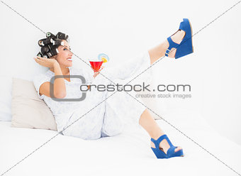 Brunette in hair rollers and wedge shoes holding a cocktail