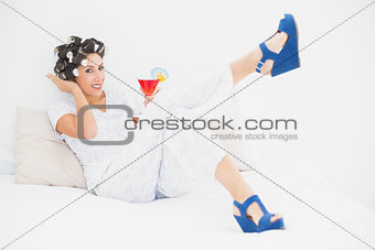 Brunette in hair rollers and wedge shoes holding a cocktail looking at camera