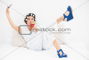 Brunette in hair rollers and wedge shoes drinking a cocktail taking a selfi