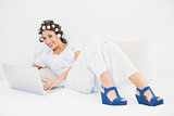Brunette in hair rollers and wedge shoes using her laptop on bed