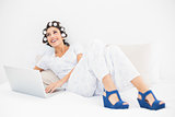 Happy brunette in hair rollers and wedge shoes using her laptop on bed