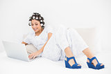 Smiling brunette in hair rollers and wedge shoes using her laptop on bed