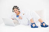 Brunette in hair rollers and wedge shoes using her laptop to shop online on bed