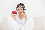 Happy brunette in hair rollers having a bowl of strawberries