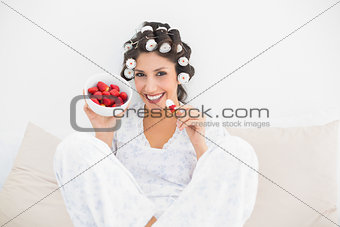 Happy brunette in hair rollers having a bowl of strawberries