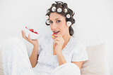 Sultry brunette in hair rollers having a bowl of strawberries