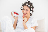 Cheerful brunette in hair rollers having a bowl of strawberries