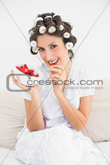 Pretty brunette in hair rollers having a bowl of strawberries