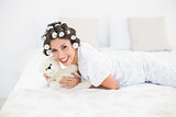 Pretty brunette in hair rollers cuddling her teddy on bed