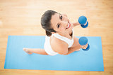 Happy woman exercising with dumbbells on blue exercise mat