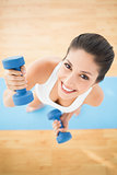 Happy woman exercising with dumbbells on blue exercise mat smiling at camera