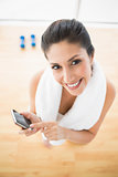 Fit woman using smartphone taking a break from workout smiling at camera