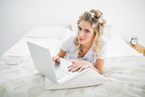 Serious pretty blonde wearing hair curlers using laptop