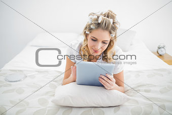 Peaceful pretty blonde wearing hair curlers using tablet pc