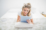Smiling pretty blonde wearing hair curlers using tablet pc