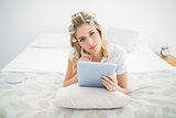 Thoughtful pretty blonde wearing hair curlers using tablet pc