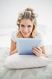 Cheerful pretty blonde wearing hair curlers using tablet pc