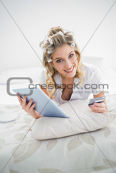 Smiling pretty blonde wearing hair curlers shopping online