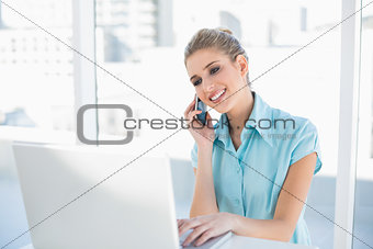 Smiling smart businesswoman on the phone while using laptop