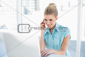 Cheerful smart businesswoman on the phone while using laptop