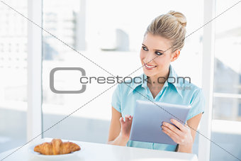 Cheerful classy woman using tablet while having breakfast