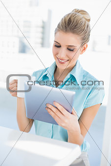 Cheerful elegant woman using tablet holding coffee