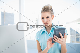 Serious elegant woman using calculator looking at laptop