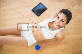 Fit smiling woman holding sports bottle lying on wooden floor