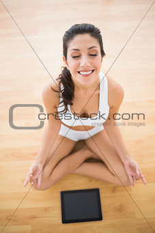 Fit woman sitting in lotus pose with her tablet pc