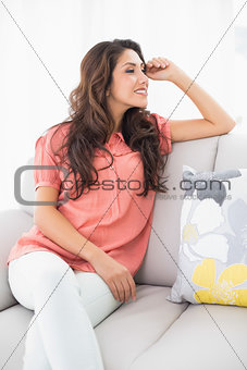 Smiling brunette sitting on her couch looking away