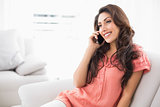 Smiling brunette sitting on her couch on a phone call