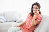 Smiling brunette sitting on her sofa on the phone