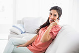 Laughing brunette sitting on her sofa on the phone looking at camera