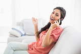 Laughing brunette sitting on her sofa on the phone
