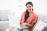 Smiling brunette sitting on her sofa using laptop