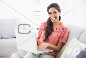 Smiling brunette sitting on her sofa using laptop