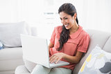 Happy brunette sitting on her sofa using laptop