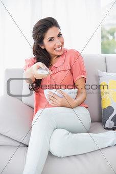Cheerful brunette sitting on her sofa watching tv holding bowl of popcorn