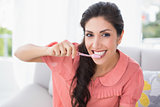 Cheerful brunette sitting on her sofa brushing her teeth