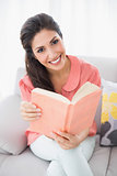 Happy brunette sitting on her sofa reading a book