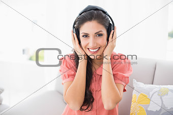 Happy brunette sitting on her sofa listening to music