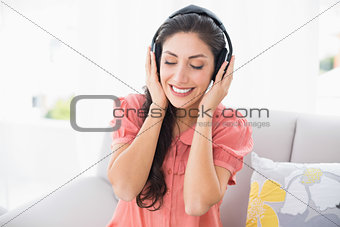 Calm brunette sitting on her sofa listening to music
