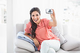 Happy brunette sitting on her sofa taking a picture of herself