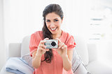 Happy brunette sitting on her sofa taking a picture of the camera