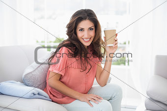 Pretty brunette sitting on her sofa holding disposable cup