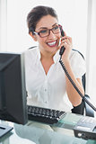Happy businesswoman sitting at her desk talking on the phone