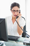 Frowning businesswoman sitting at her desk talking on the phone