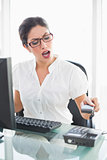 Angry businesswoman sitting at her desk hanging up the phone