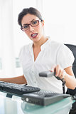 Offended businesswoman sitting at her desk hanging up the phone